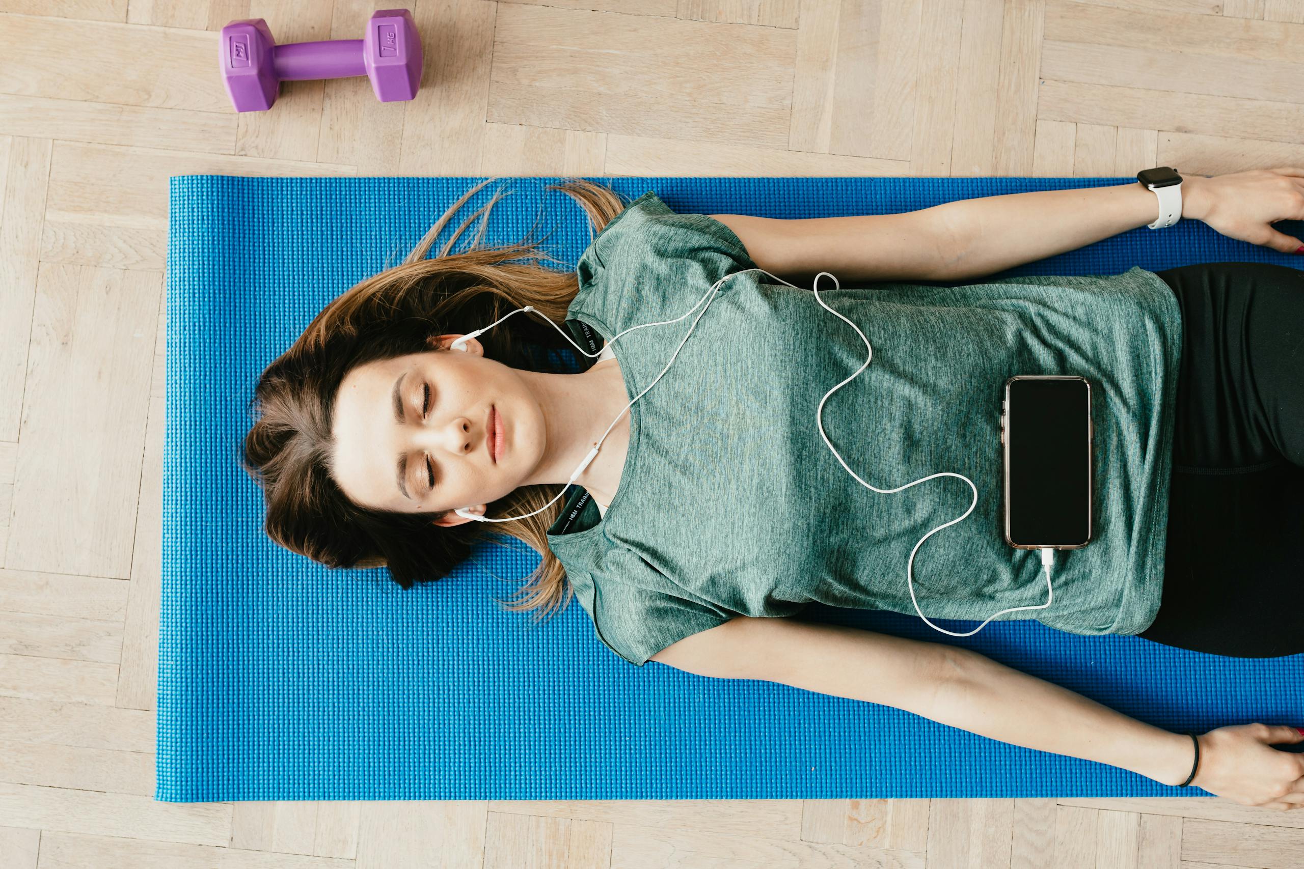 Peaceful woman in earphones resting in Shavasana pose at home